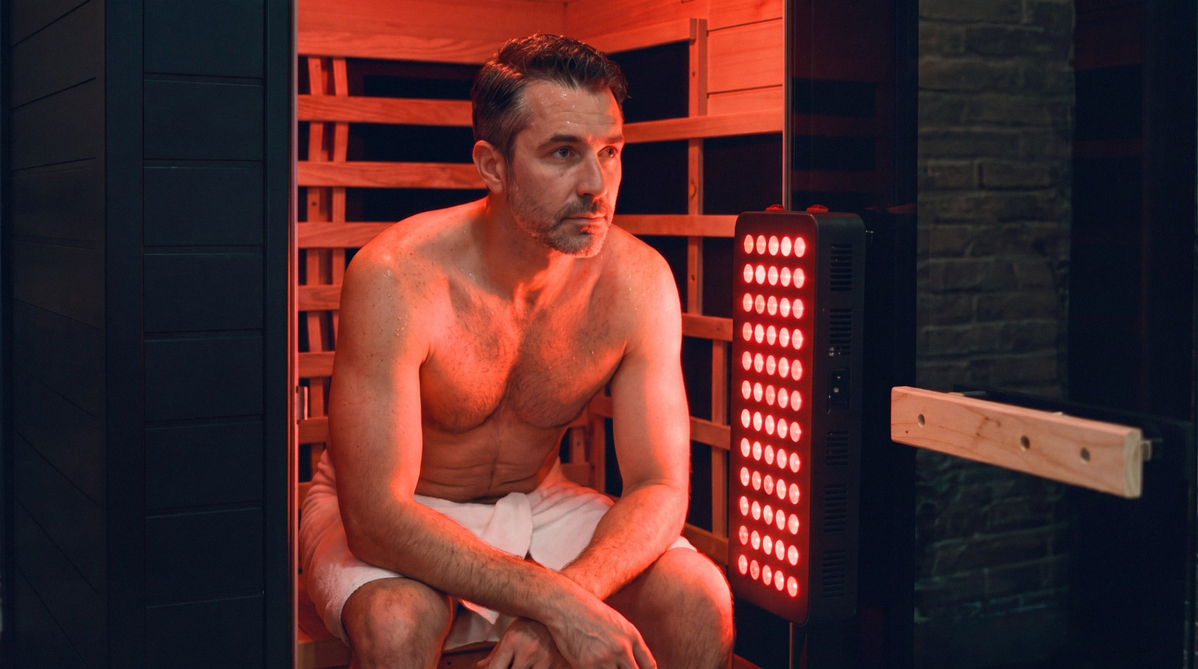 Man sitting in a SaunaBox Solara in the evening with the red light panel on