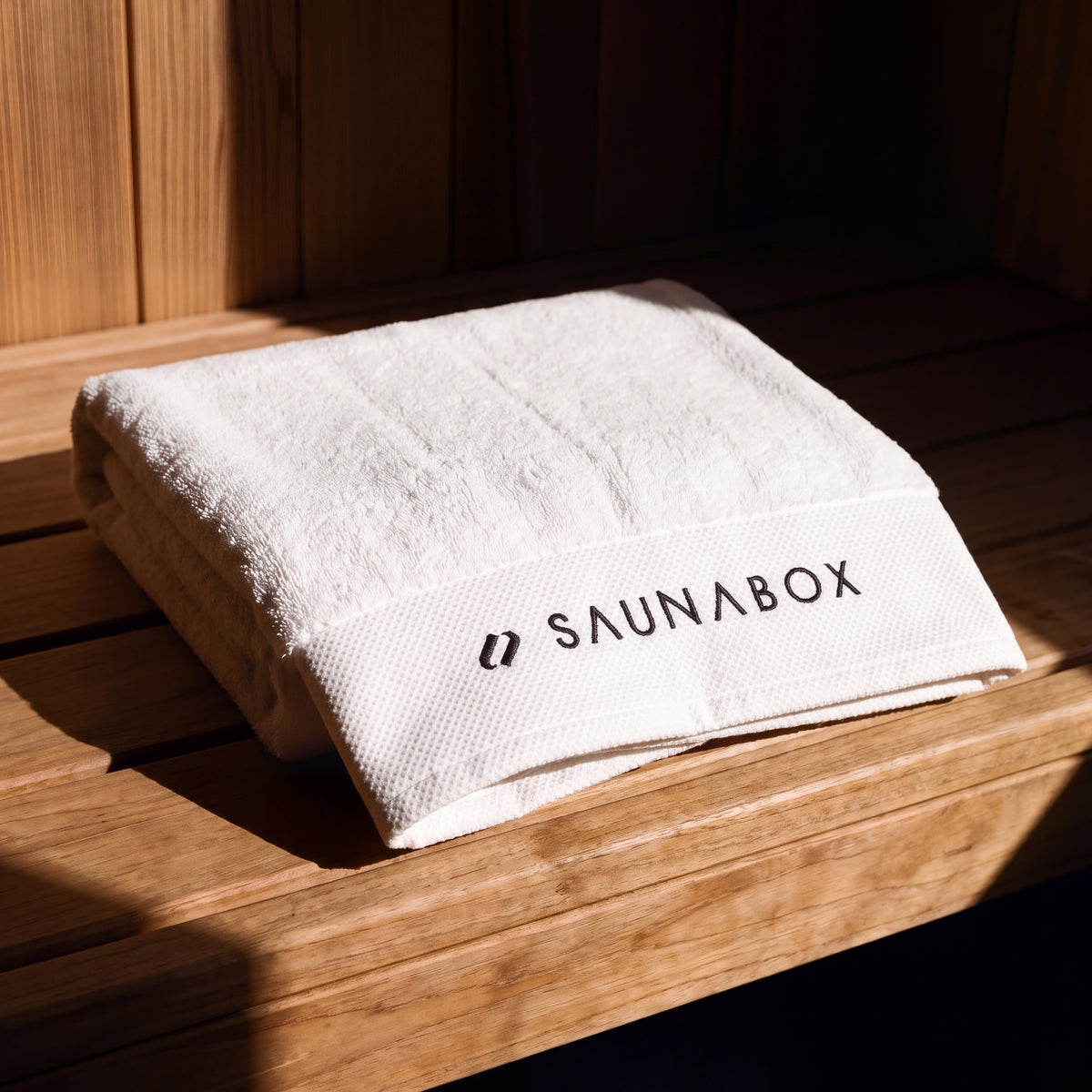 SaunaBox 100% cotton full body towel, single towel folded on a cedar sauna bench